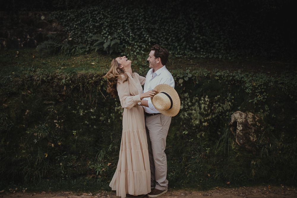 A couple in neutral colors sharing a romantic moment against a lush green backdrop.