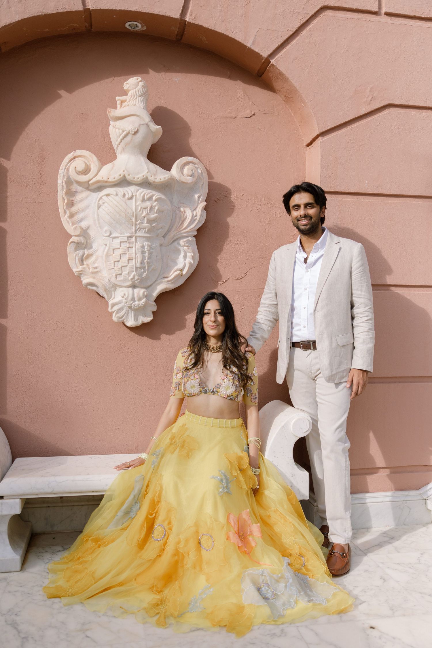 Elina and Jag beside a marble bench against the pink palace wall at Villa Padierna.