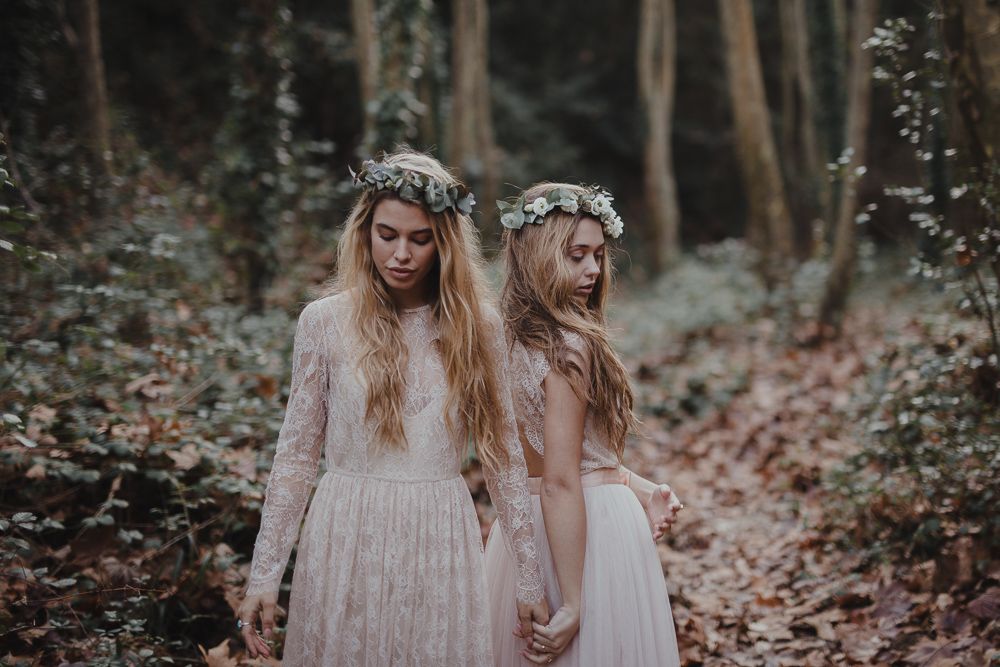 Two people in ethereal dresses and flower crowns pose in a misty autumn forest.