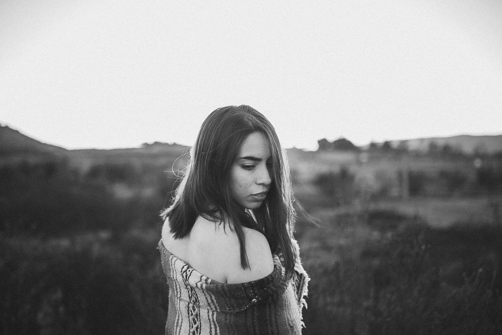 A moody black and white portrait showing someone looking down while wearing an off-shoulder top.
