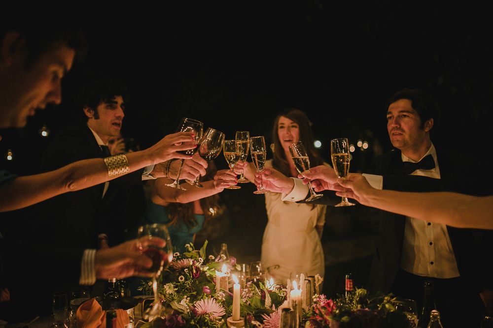 Wedding guests raise their glasses for a celebratory toast at a candlelit reception.