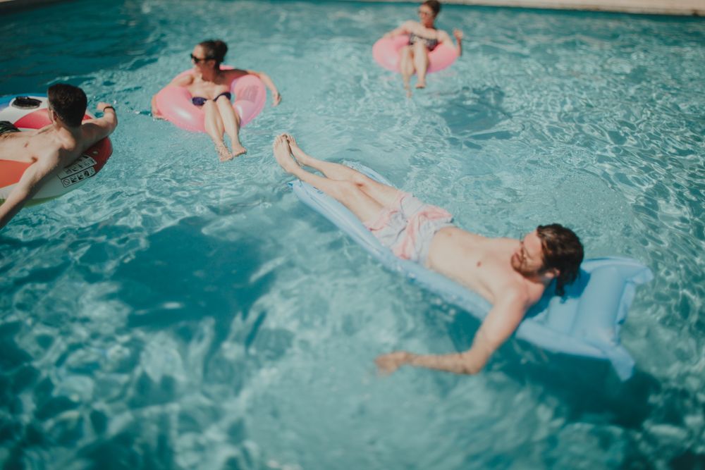 People floating and relaxing in blue swimming pool water.