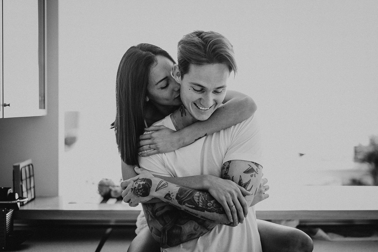 Affectionate embrace captured in black and white photography in a modern kitchen setting.