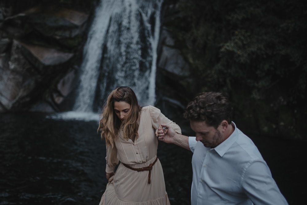 A romantic moment captured between a couple near a waterfall as they balance on rocky terrain.