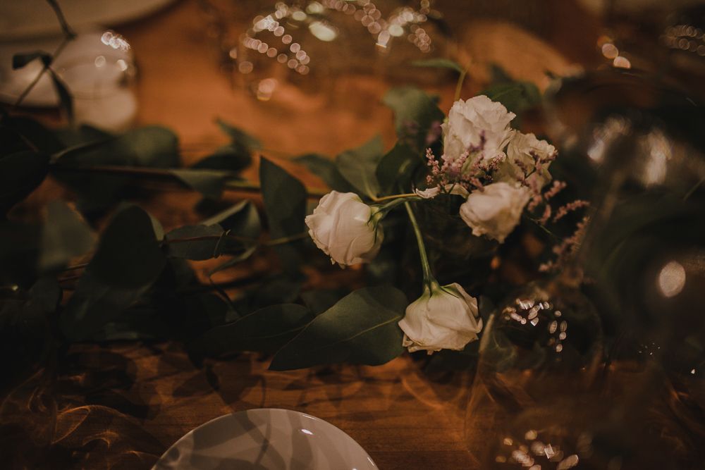 White roses and greenery in moody lighting create a romantic table setting.