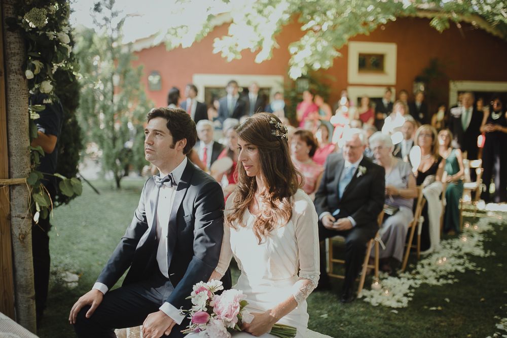 Outdoor wedding ceremony under trees with red barn backdrop and seated guests.