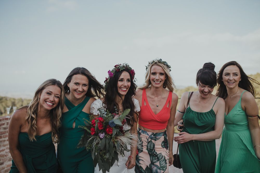 Wedding party in green dresses and floral arrangements posing outdoors.