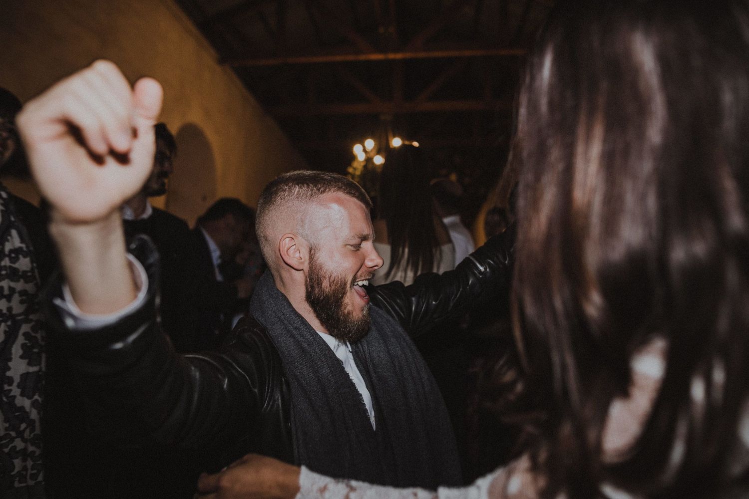 Wedding guest dances energetically with fist raised at indoor reception celebration.