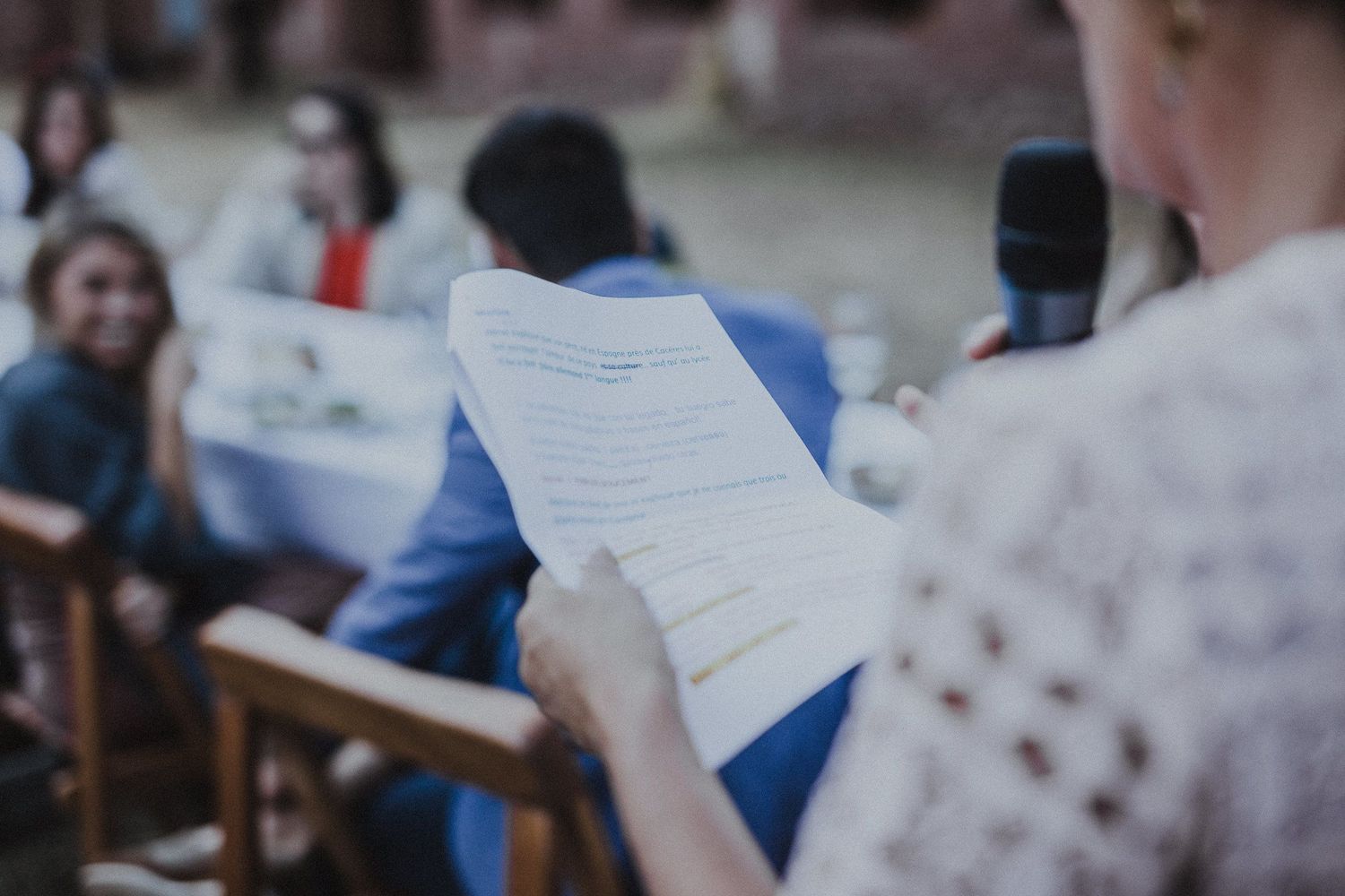 Someone holds a paper document during outdoor gathering with people seated on benches.