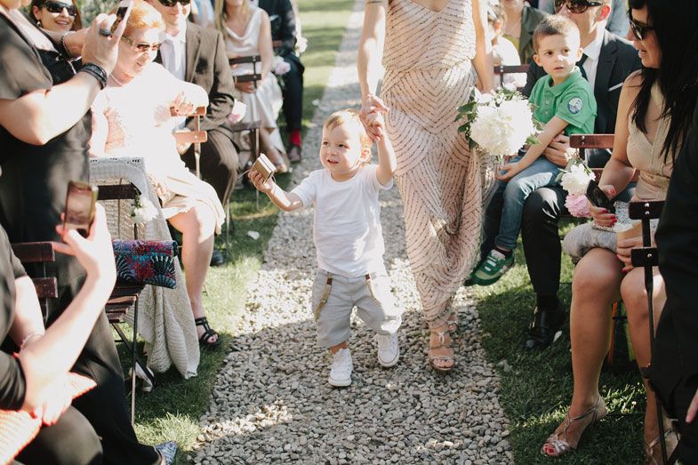 Young children walking down aisle at outdoor wedding while guests look on.