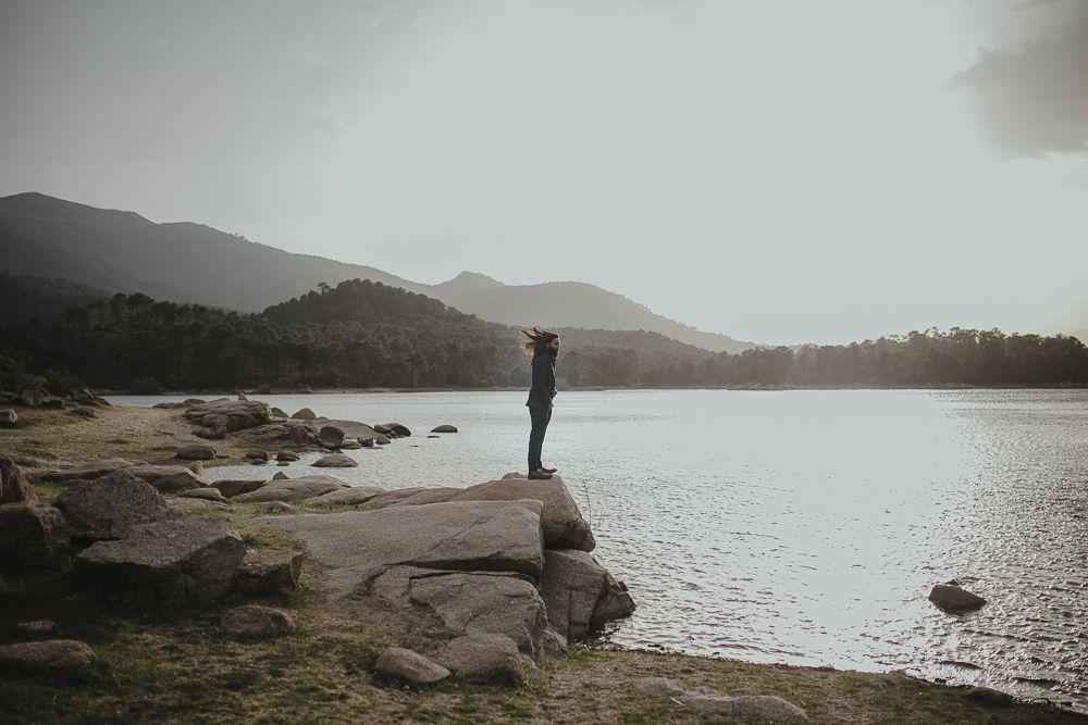 Silhouette standing on rocky cliff overlooking a serene mountain lake at dusk.