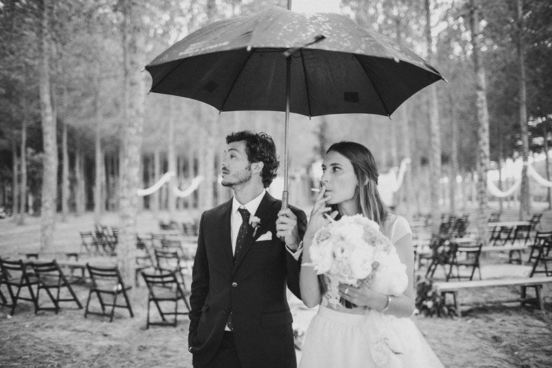 Couple shelters under a black umbrella at their forest wedding ceremony site.
