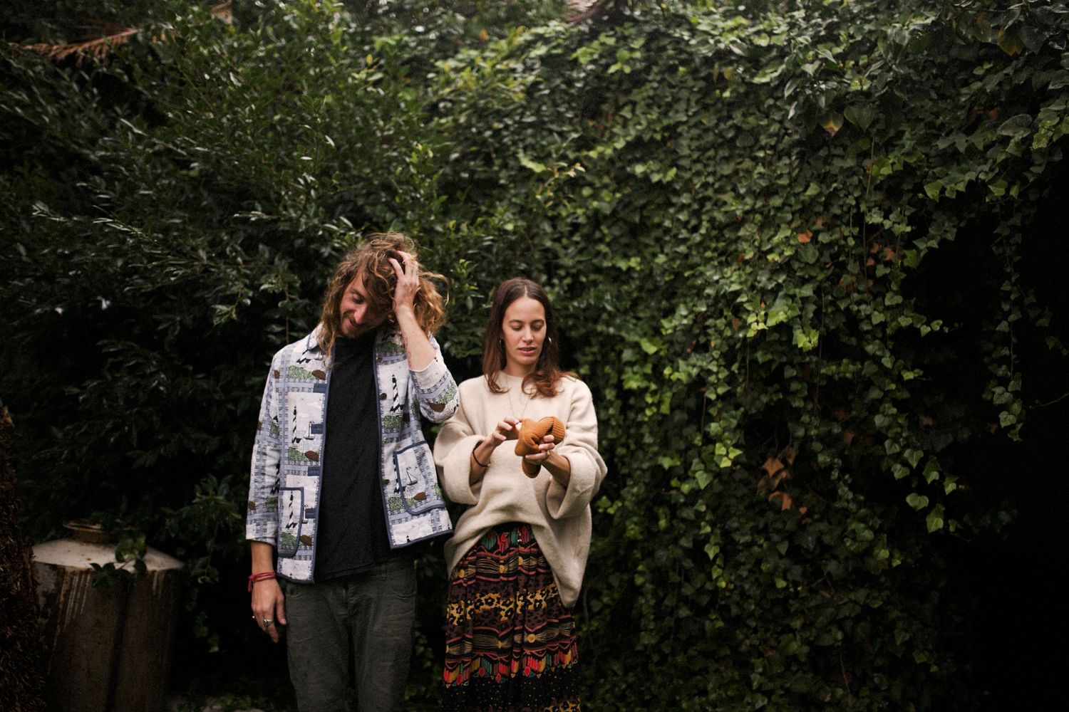 Two people standing in lush garden setting with green foliage background.