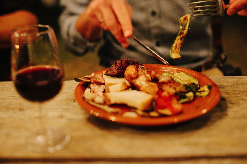 Plate of Mediterranean food with wine glass on wooden table in warm lighting.