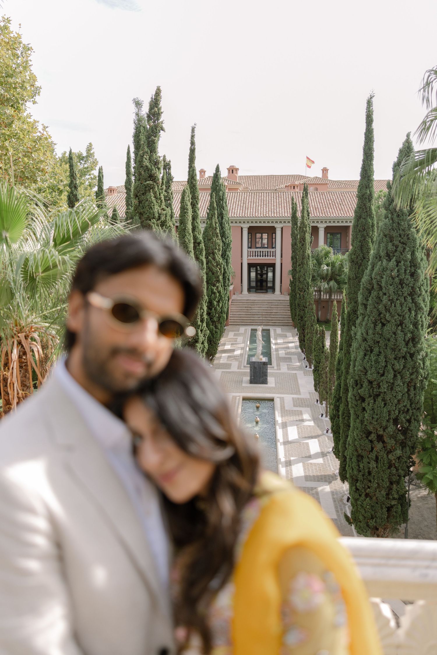 Soft-focus portrait of Elina and Jag with the cypress-lined garden behind them.