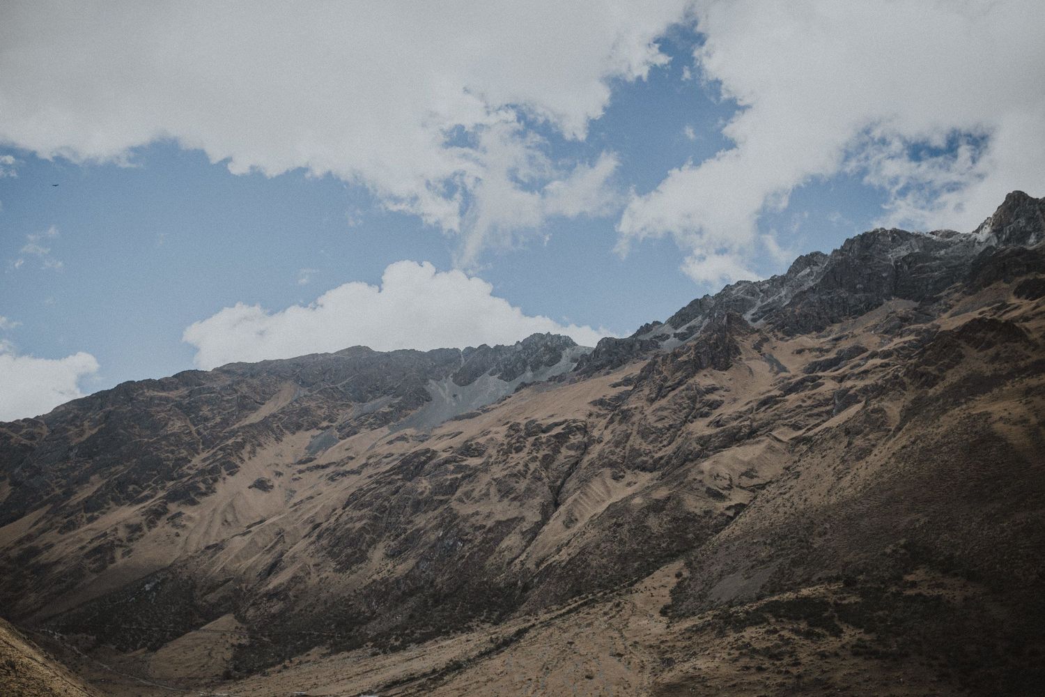 Rugged mountain peaks rise against a bright blue sky with scattered white clouds.