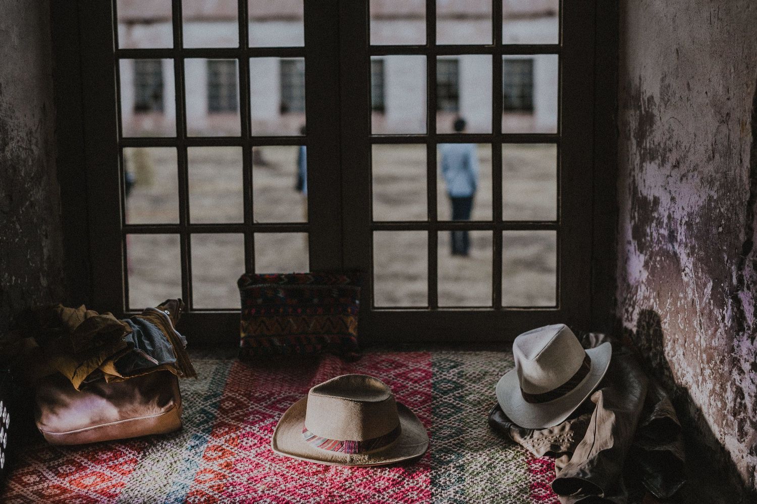 Hats and accessories arranged on a patterned rug by a window in vintage setting.