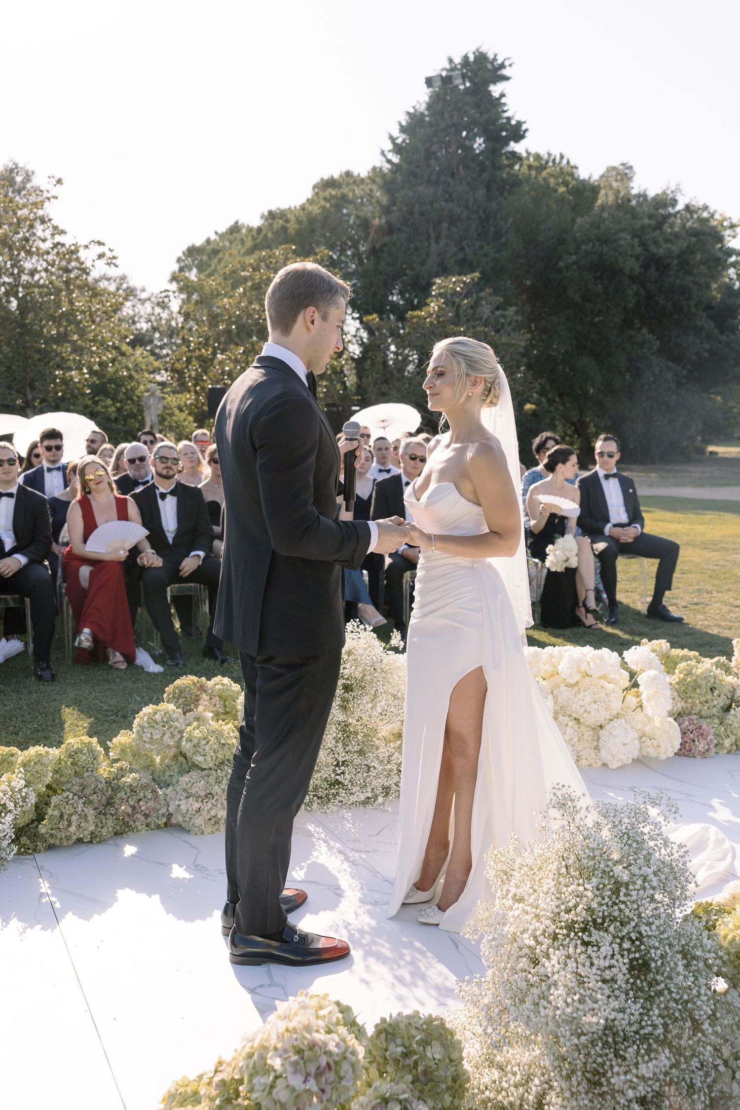 Outdoor wedding ceremony with elegant white floral arrangements and guests seated on the lawn.