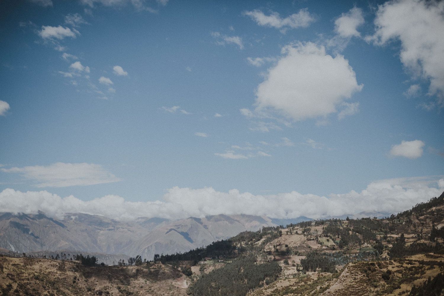 Dramatic mountain landscape with rugged peaks and valleys under bright blue sky with scattered clouds.