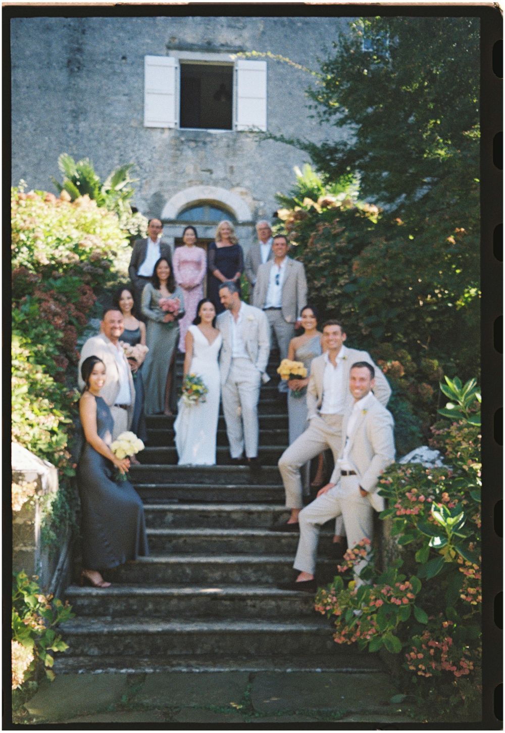 Wedding party poses on stone steps surrounded by lush greenery.