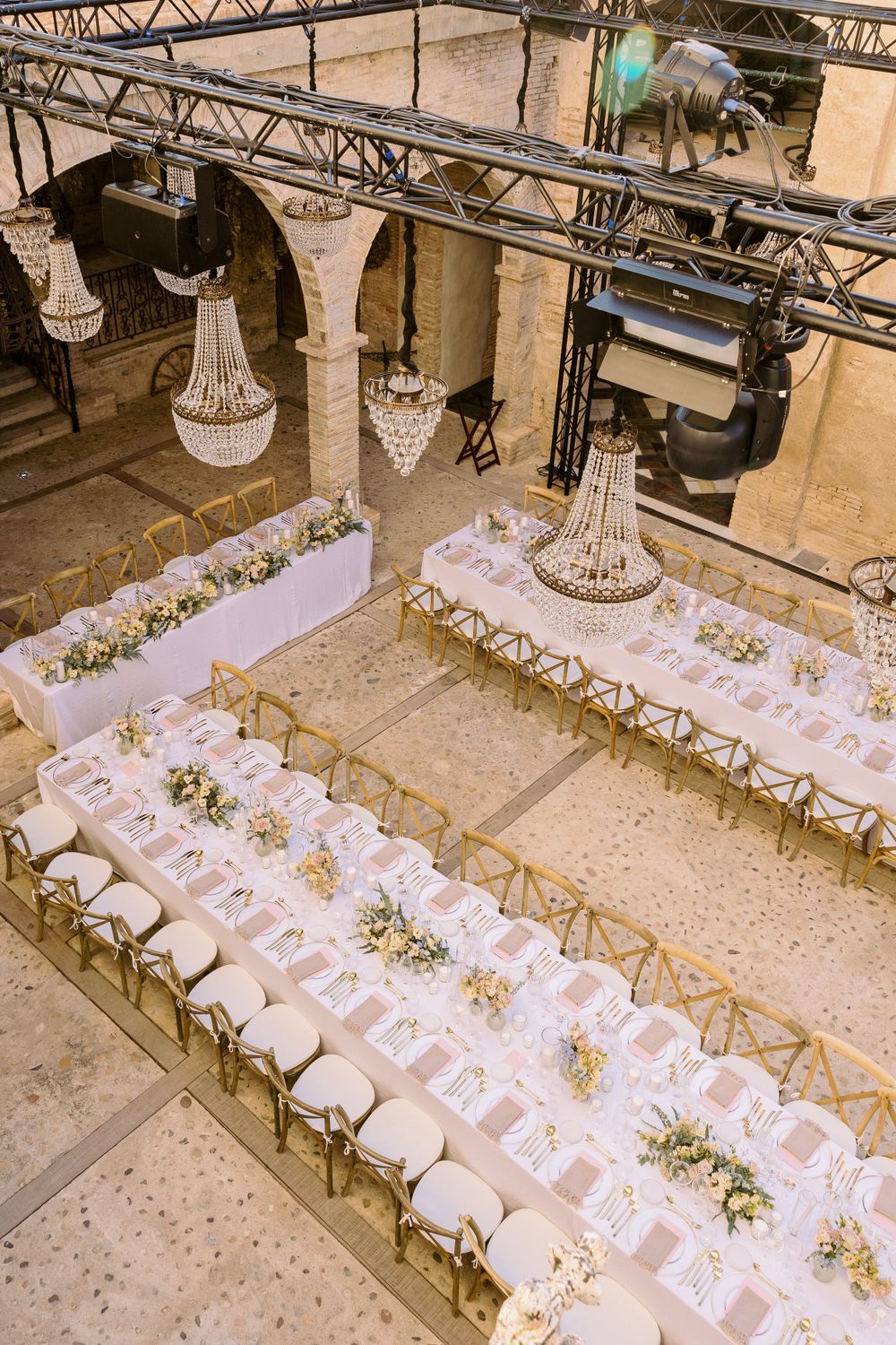 Elegant wedding reception setup with long tables and white chairs arranged under industrial beams.