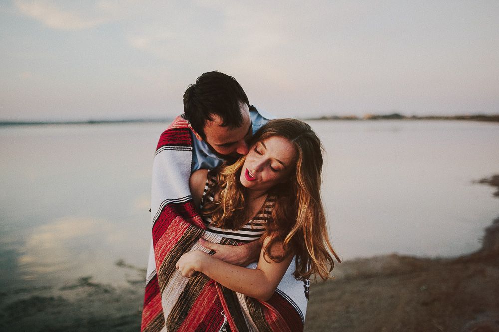Intimate couple moment shared under cozy blanket near peaceful waterfront.