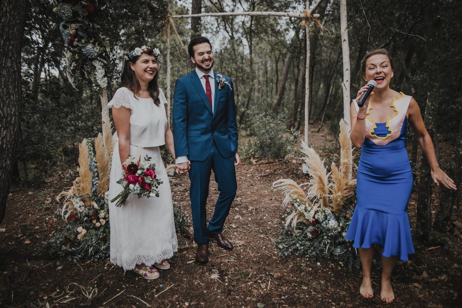 A wedding party poses together in a forest setting wearing formal attire.