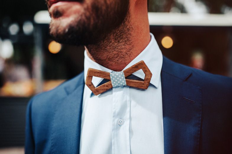 Close-up detail of a wooden and patterned bow tie worn with a navy blue suit.