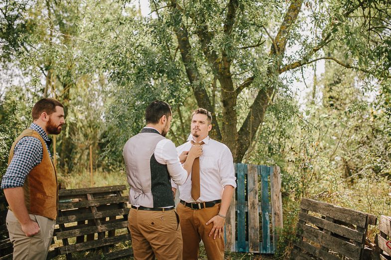 Groomsmen in rustic attire gather outdoors for pre-wedding preparations.