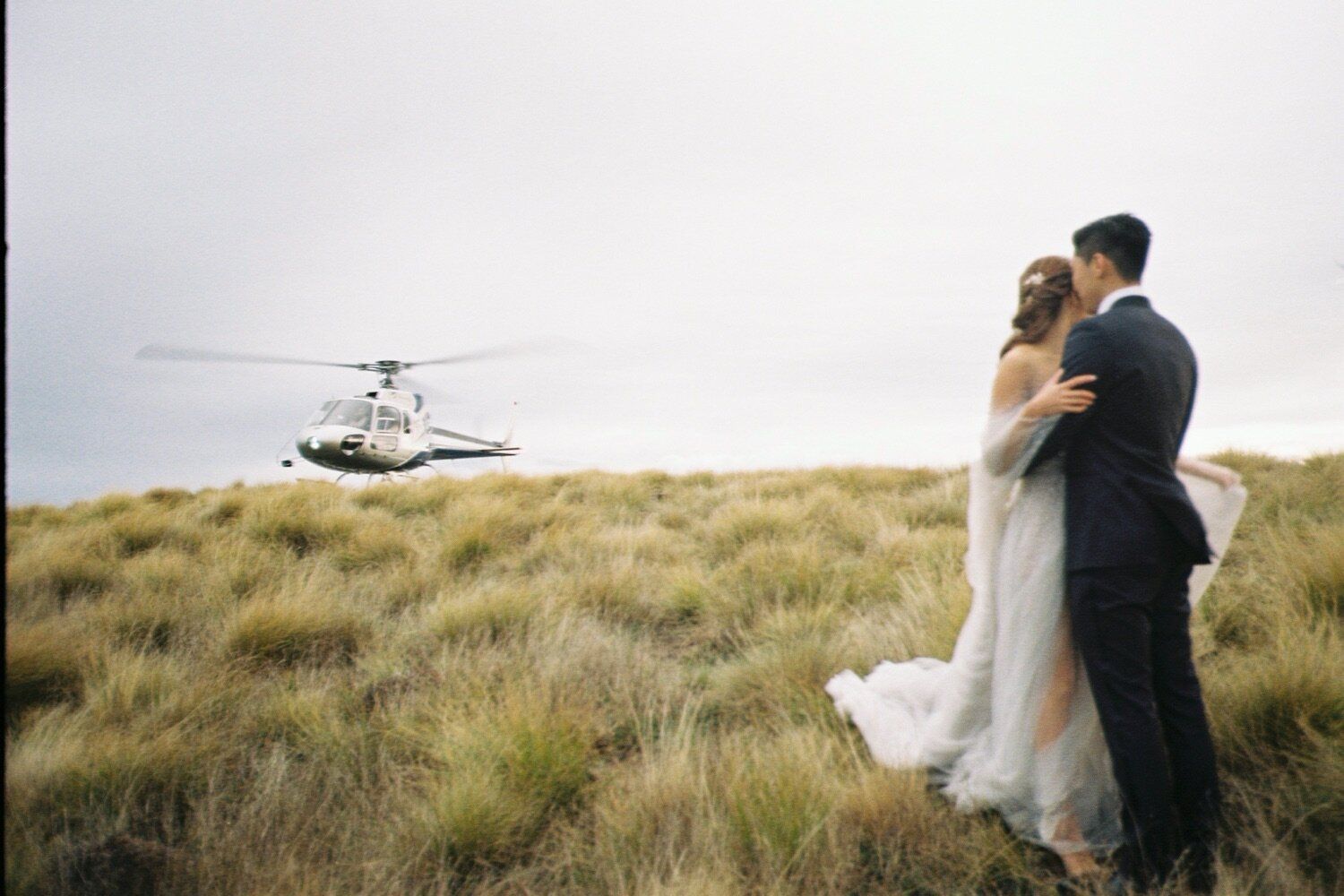 Helicopter approaches mountain summit during dramatic wedding photo shoot.