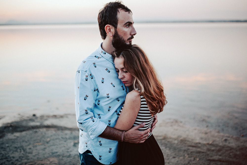 A tender embrace between a couple at dusk near a serene waterfront.