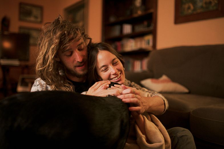 Candid moment of joy and laughter shared on dark couch in warm-lit living room.