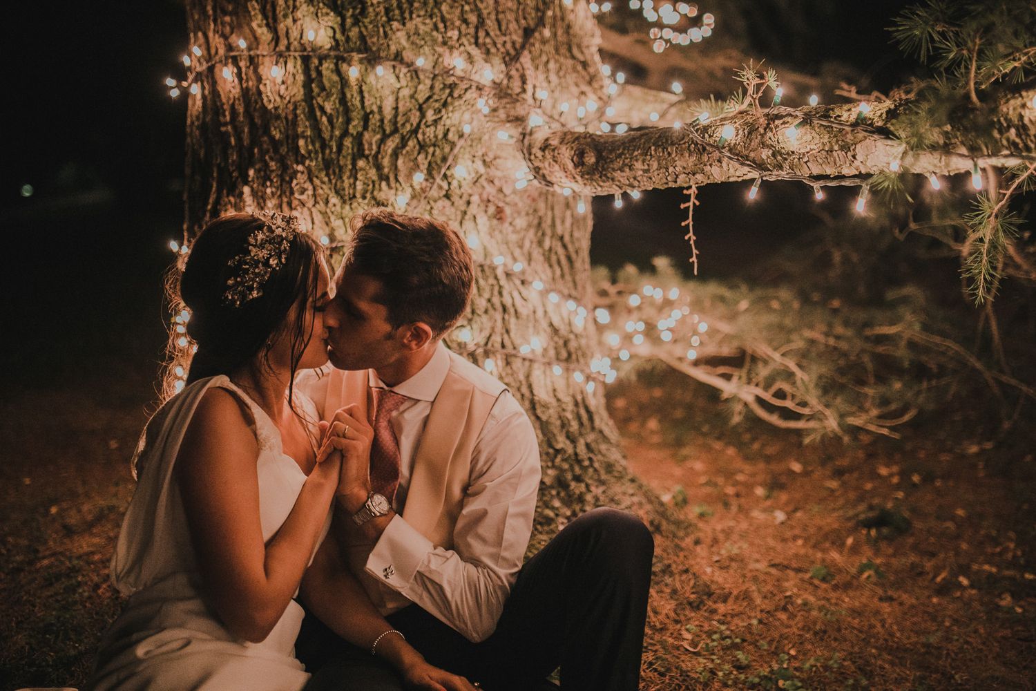 A couple shares a romantic moment under twinkling lights in a rustic outdoor setting.