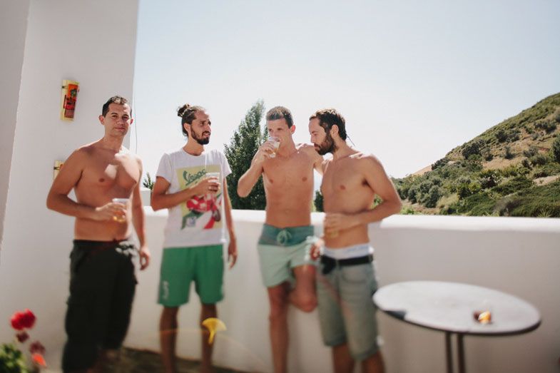 Group of shirtless friends socializing on a white terrace with scenic mountain backdrop.