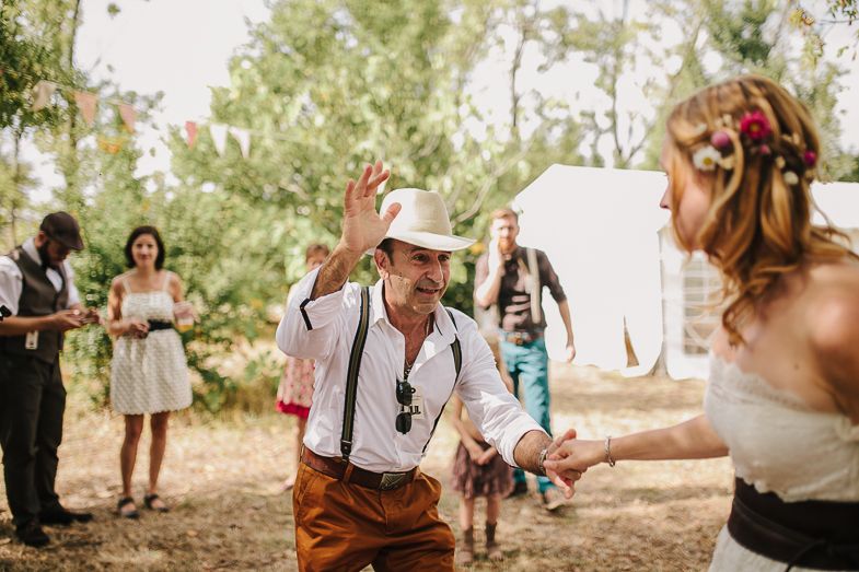 Guests dancing at a festive outdoor wedding celebration under trees.