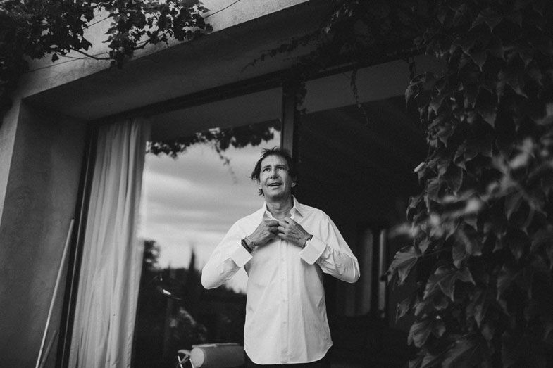A black and white photo of someone adjusting their collar by a window.