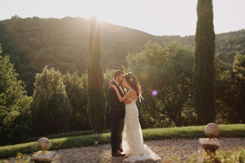 A wedding couple embraces during golden hour in a Tuscan garden with cypress trees.