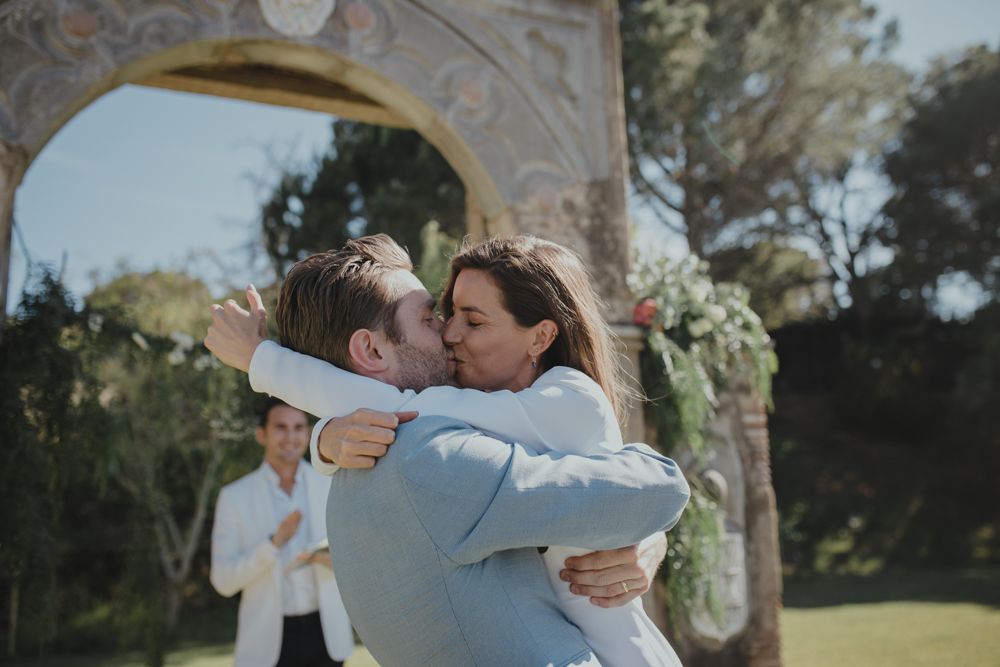 Romantic wedding couple embraces under stone archway during ceremony.