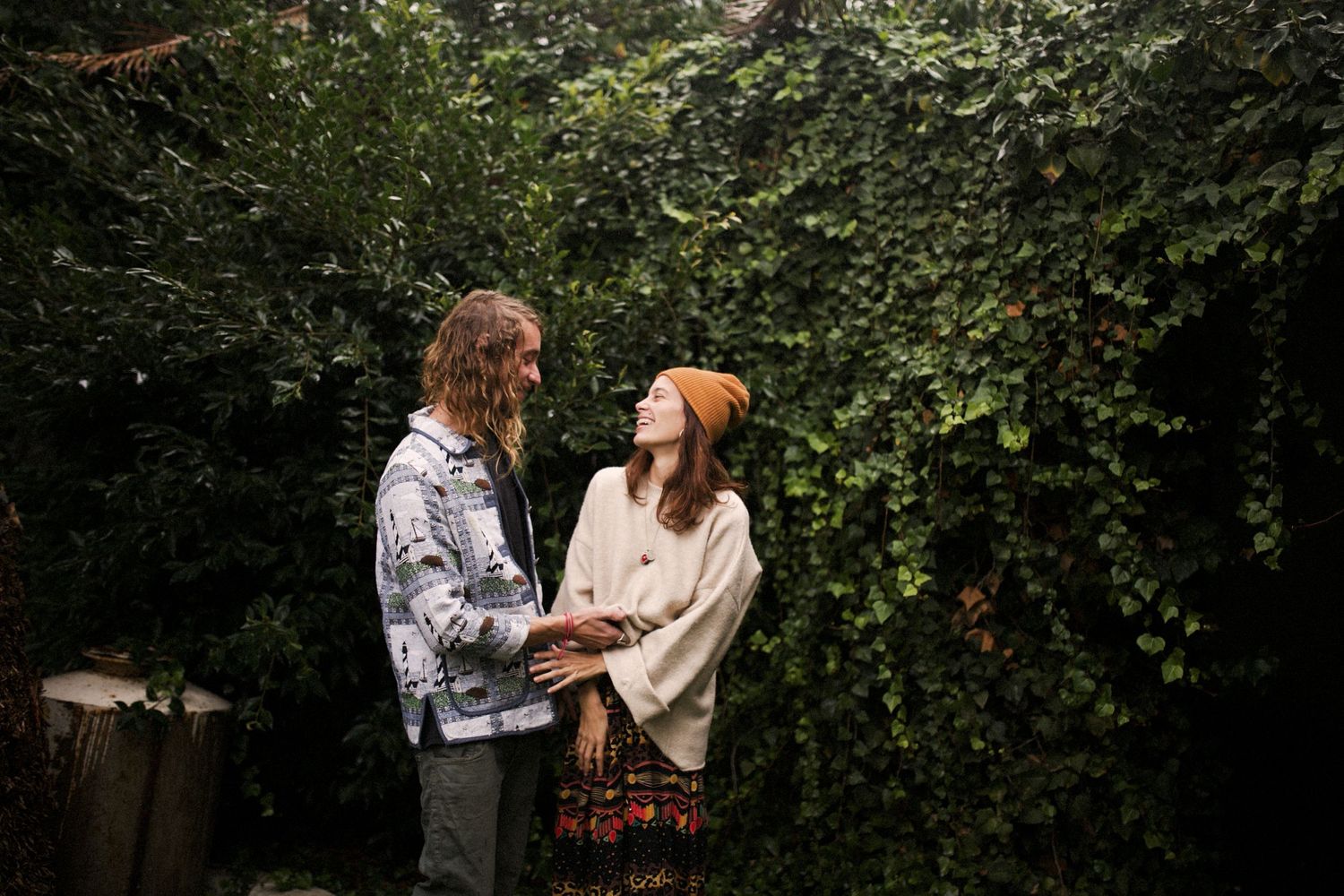 Casual couple sharing a moment together in front of green garden foliage.