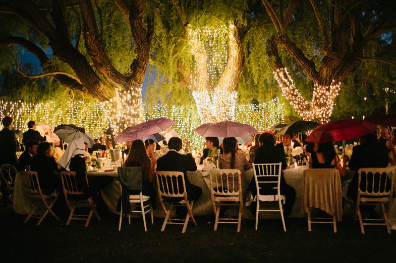An enchanting outdoor wedding reception with string lights illuminating tables under large trees.