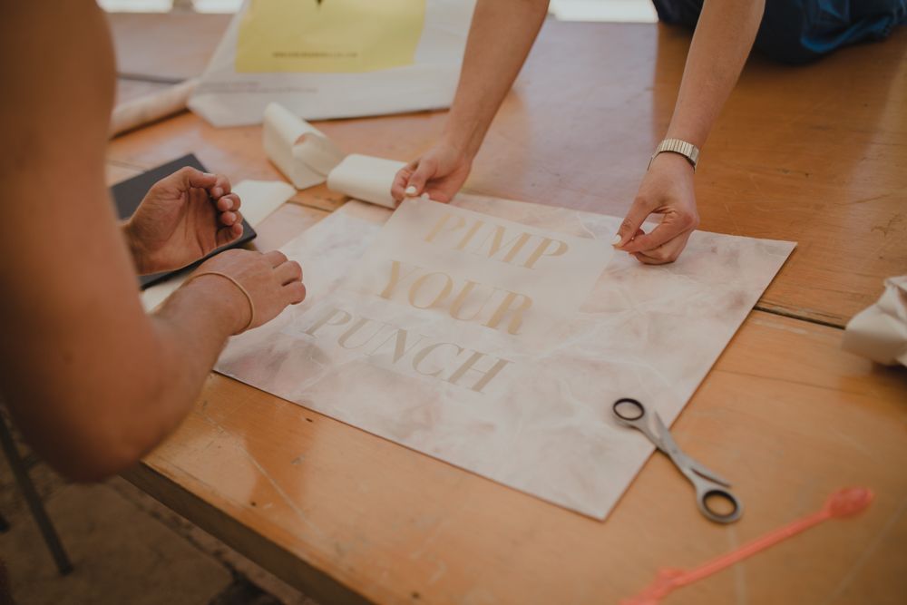 Hands working on a DIY wedding craft project with paper and scissors on wooden table.