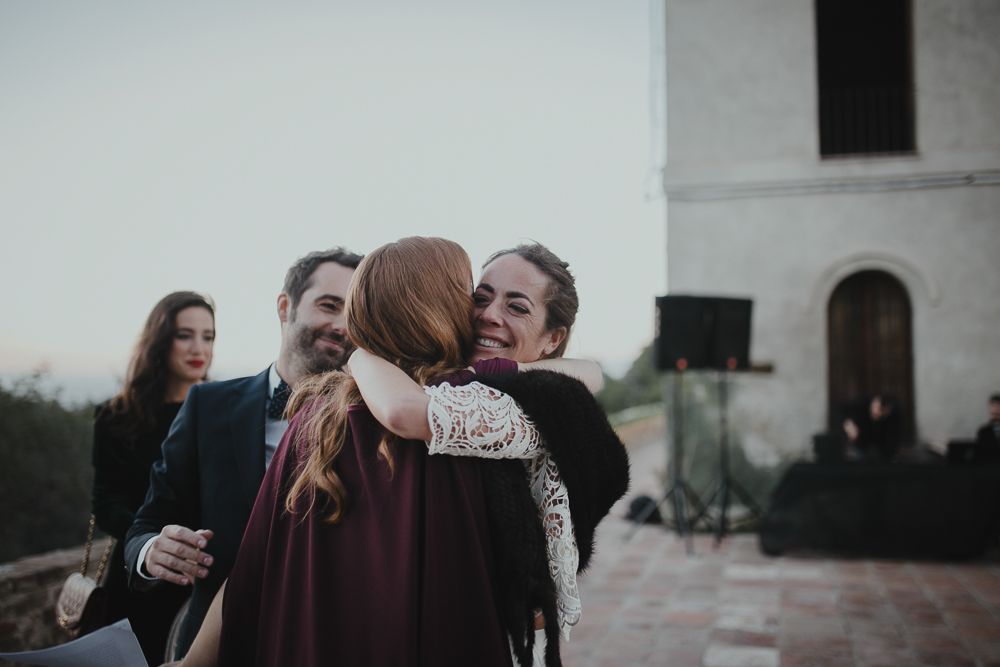 A group embraces warmly at an outdoor wedding celebration near a white building.