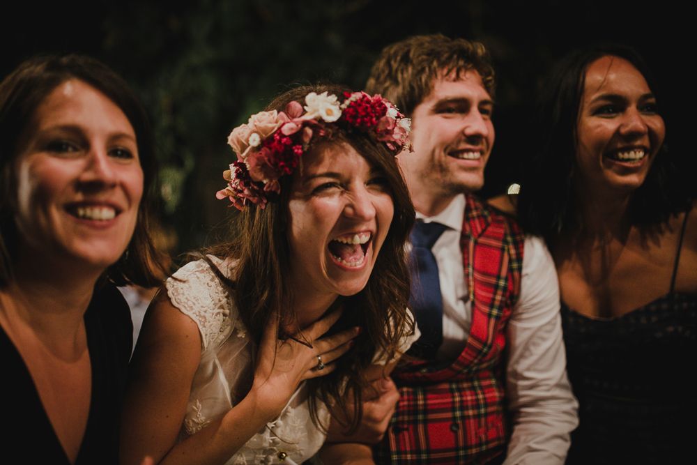 Wedding party laughs together during evening celebration with festive decorations.