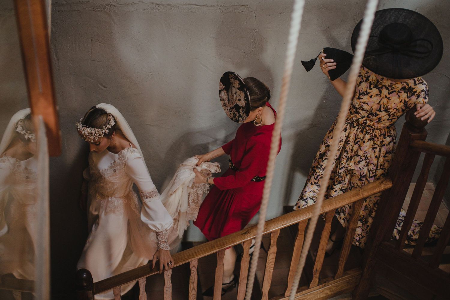 Wedding party descends staircase in elegant white and floral dresses during ceremony preparations.