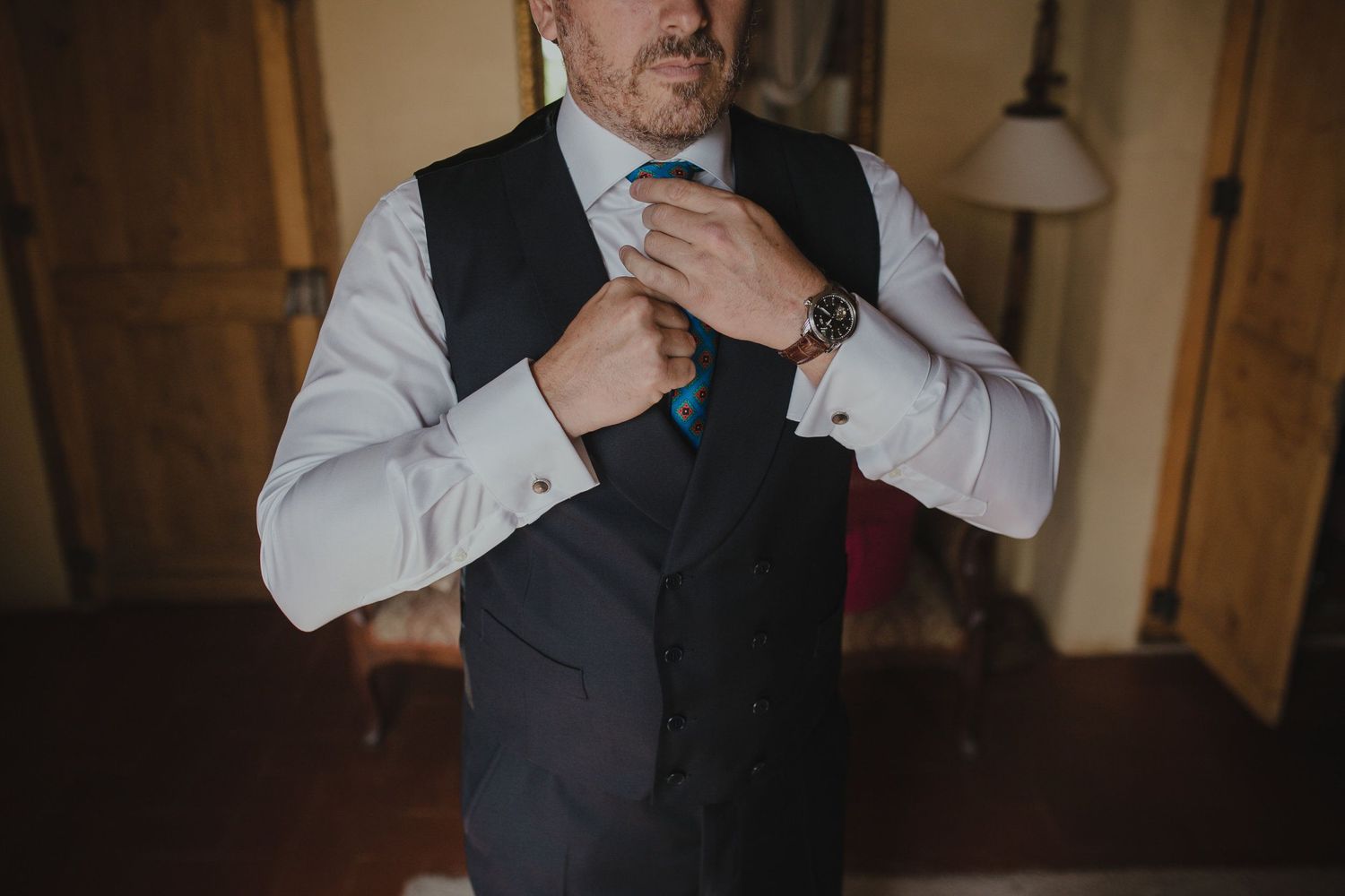 Close-up shot of someone adjusting a black vest and tie while getting dressed.