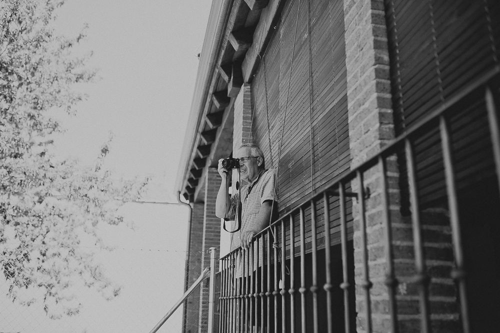 Black and white image of someone looking through window blinds on building exterior.