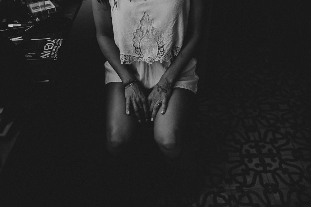Close-up black and white shot of someone wearing a delicate lace top with hands folded in their lap.
