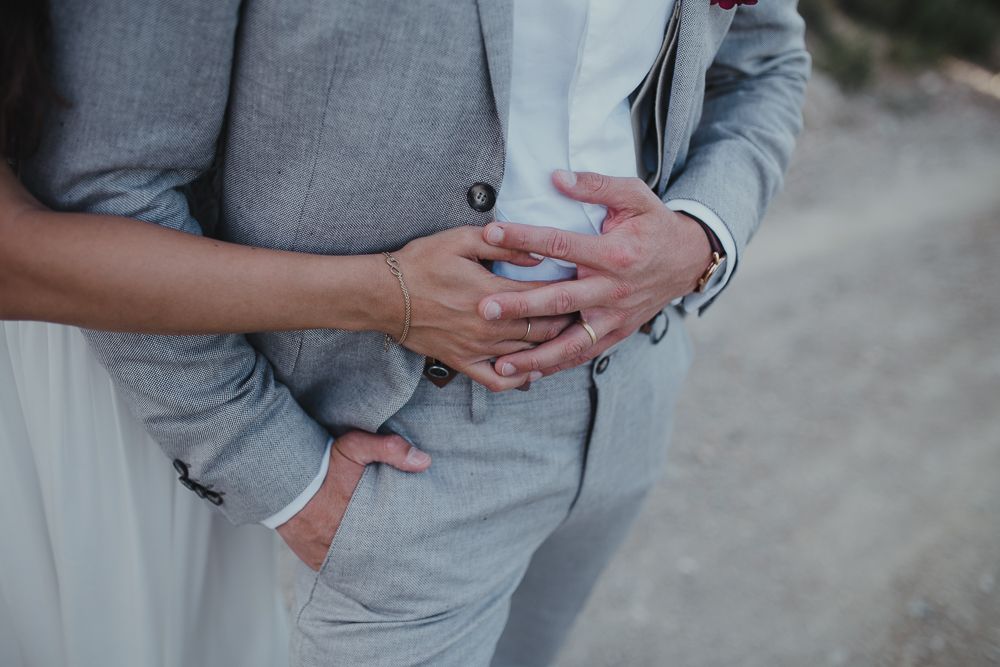 Close-up shot of couple's hands embracing while wearing wedding attire.