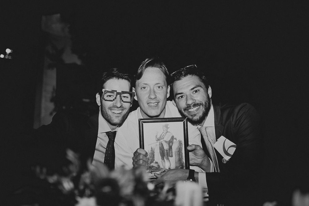 Three people smiling while holding a framed photo at a party celebration in black and white.