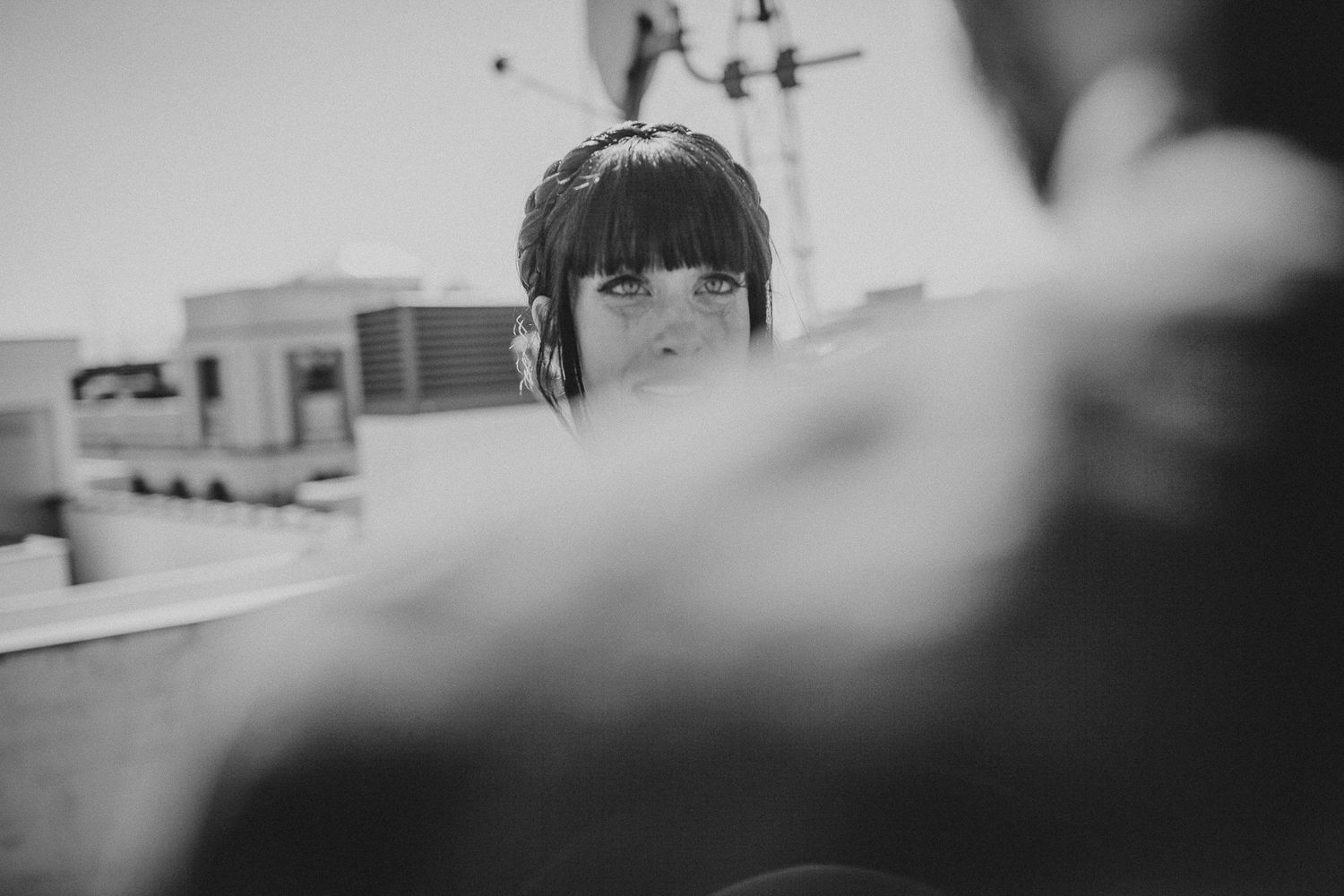 Artistic black and white photograph of a woman with bangs in a white dress on a city rooftop.